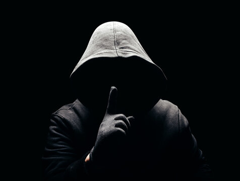 Photo of a scary horror man in hoodie showing silence hand sign in dark.