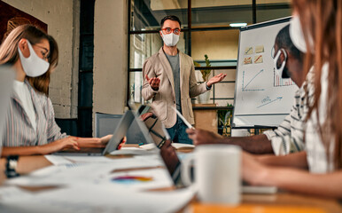 Workers discuss and meet while wearing a medical mask to protect against the corona virus. A young man writes a mind map on a whiteboard and makes new business plans during the COVID-19 pandemic.