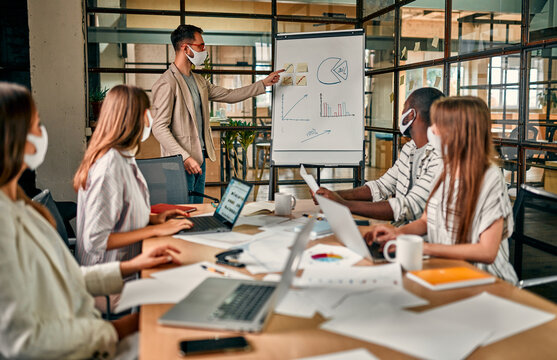 Workers discuss and meet while wearing a medical mask to protect against the corona virus. A young man writes a mind map on a whiteboard and makes new business plans during the COVID-19 pandemic. - Powered by Adobe