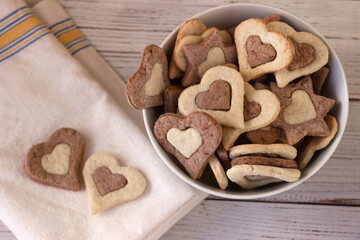Shortbread cookies of two colors in a white plate on a wooden background. Sweet cookies in the form of hearts for February 14 (Valentine's Day)