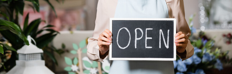 partial view of florist holding board with open lettering near plants on blurred background, banner