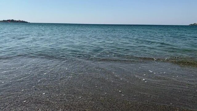 Footage of little waves of Aegean sea at "Akarca" beach in touristic Aegean town called "Sigacik". It is a village of Seferihisar district of Izmir / Turkey. It is a sunny summer day.