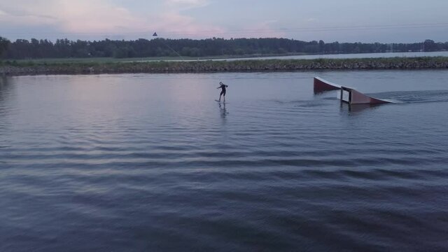Aerial drone footage of a wakeboarder at a wakeboard cable park ride and does at trick out of a kicker in southern sweden bromölla during a summer evening sunset