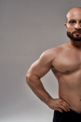 Fototapeta na wymiar Personal fitness trainer. Half face portrait of young muscular bearded man bodybuilder with naked torso looking at camera while standing isolated over grey background