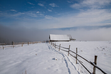 Long winding old wooden fence on a snowy hill in dense fog. Selective focus. Blurred background.