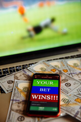 Smartphone with gambling mobile application on dollar banknotes and laptop with football match online broadcast.