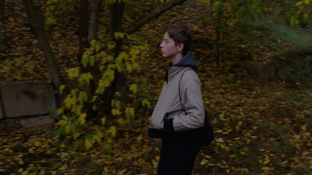 A boy walking along a country road in the autumn nature. autumn walk, Cute boy with backpack goes to school in the suburbs. High quality 4k footage