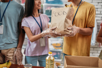 Cropped shot of male and female volunteers holding paper bag with food while packing donation for...