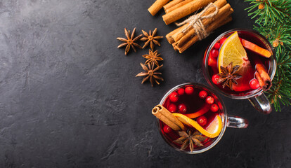 Hot wine with spices and fruits in a glass on a black textured background and branches of a Christmas tree, top view. Alcoholic hot drink for the holiday.