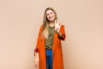 blonde woman smiling and looking friendly, showing number four or fourth with hand forward,...