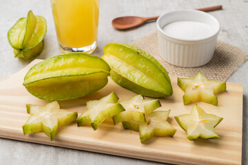 Starfruits with slices and juice over a wooden plate