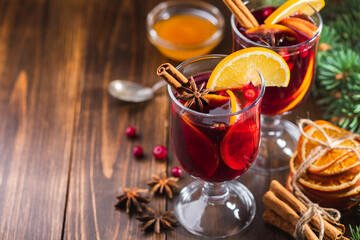 Hot wine drink with spices and fruits in a tall glass and branches of a Christmas tree on a wooden background, copy space. Christmas mulled wine or punch.