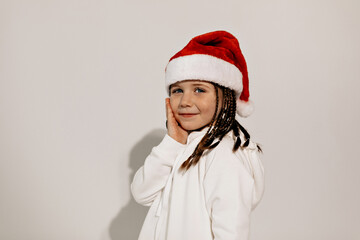 Close up studio shot of adorable cute little girl in santa hat and white dress posing on isolated background, New Year, christmas mood