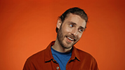 Fototapeta premium joyful and bearded man smiling while looking away on orange