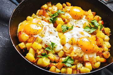 Potato hash with eggs and herbs for breakfast on black stone background
