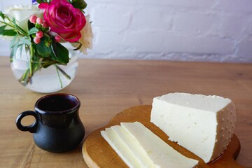 Homemade feta cheese and black cup of coffee on a wooden tabletop. Concept on the background of a white brick wall and a bouquet of roses.