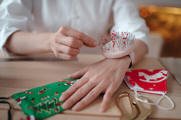 Close-up. A seamstress girl sews a homemade protective medical mask with a New Year or Christmas print. Pin cushion on the arm