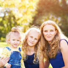 Fototapeta premium Mother and little daughters. Happy family portrait. Mom hug. Outdoor lifestyle. Cute face. Smile positive parent. Female child love. Green background. Baby girl. Casual cloth