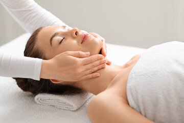 Obraz na płótnie Canvas Joyful young woman relaxing during face lifting massage