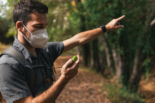 Man looking at the GPS pointing out the direction of the right route while hiking in the mountain with a mask on the covid-19. Concept of sport. Nature and environment