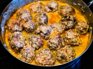 meatballs are stewed in tomato and cream sauce in saucepan at home kitchen