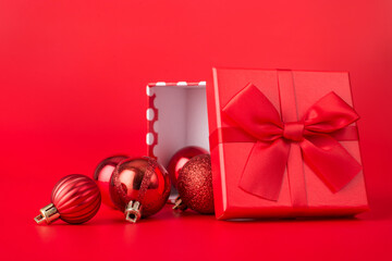 Holiday decorations and presents concept. Close up photo of red decorated baubles and an open red giftbox with red ribbon isolated on red background