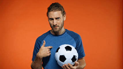 football fan in blue t-shirt holding soccer ball and pointing at himself on orange