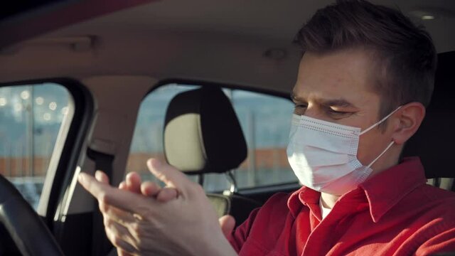 Man wearing mask in car desinfecting his hands to protect from coronavirus. Wearing protection masks man sanitizing stearing wheel during the second wawe coronavirus COVID19. Car Wash or carsharing
