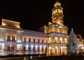 Fototapeta na wymiar Christmas tree and new year decorations in front of the town hall building, at night, in the city center of Arad, Romania