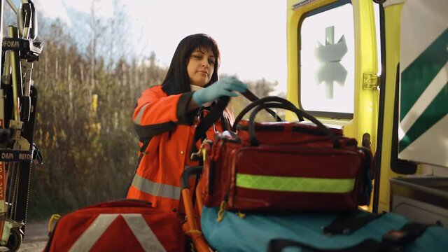 Female paramedic grabs large equipment bag and leaves emergency vehicle