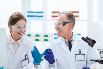 smiling scientists with a Petri dish sitting at a laboratory table.