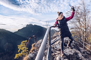 A smiling tourist takes a selfie on mountain peak.