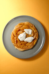 Top Shot von Apfel Tarte Tatin mit Créme Fraiche auf grauem Teller mit gelbem Hintergrund