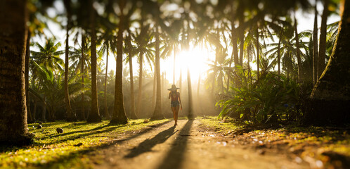 Silhouette of a beautiful girl wearing a large hat and a red bikini walking on a pathway surrounded...