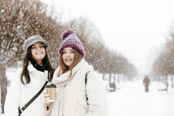 Fototapeta na wymiar Female friends posing with hot coffee during snowfall