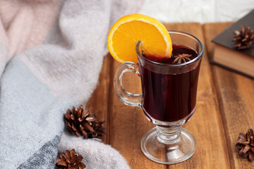 Mulled wine with cinnamon and anise, garnished with orange on a wooden background with pine cones...