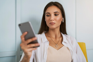 Obraz premium Beautiful brunette woman using smartphone, writes messages, shares photos, chatting with friends, checks email