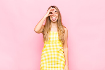 blonde woman smiling happily with funny face, joking and looking through peephole, spying on secrets