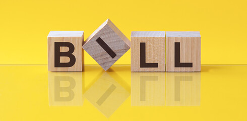 bill word is made of wooden building blocks lying on the yellow table, concept