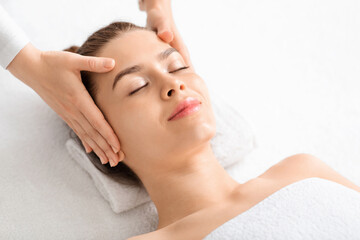 Fototapeta na wymiar Joyful young woman relaxing during face lifting massage, copy space