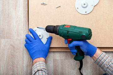 Man in gloves assembles table furniture with drill. Assembly, furniture repair home master. Male hand with drill on floor. Top view