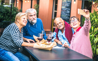 Happy senior friends taking selfie at restaurant - Retired people having fun together with mobile phone - Positive elderly lifestyle concept