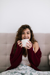 portrait of a white girl with brackets and curly brown hair holding a cup of breakfast while looking at the camera smiling