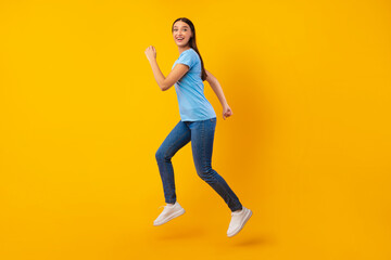 Fototapeta na wymiar Happy lady jumping and running over yellow studio wall