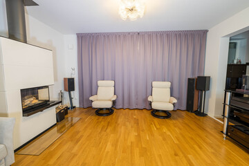 Fototapeta na wymiar Beautiful interior view of modern decorated room in private home. White fire place , hi-fi speakers and light colored furniture on purple curtains background.