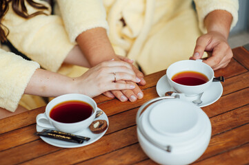 A loving couple sits in dressing gowns and drinks tea on a wooden table