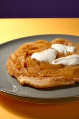 Apfel Tarte Tatin mit Créme Fraiche auf grauem Teller mit gelbem Hintergrund