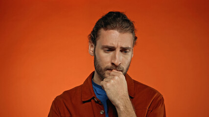 young pensive man thinking on orange background