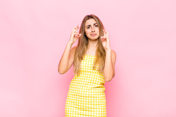 blonde woman crossing fingers anxiously and hoping for good luck with a worried look