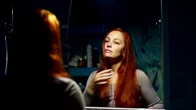 red-haired woman combs her hair in the bathroom by the mirror